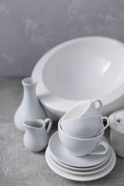 Boş çanak çömlek seti ya da beyaz seramik tabaklar. Beyaz mutfak bulaşık takımı ve sofra takımı gri duvar arkaplan dokusunun yanındaki masada.