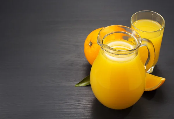 Jarro de vidro e suco de laranja na madeira — Fotografia de Stock