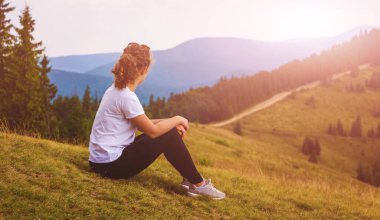 Genç bir kız dağın yamacında oturur ve güneşin doğuşunu seyreder.