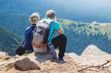 Genç adam ve kız dağın tepesinde oturuyor ve doğaya hayran.