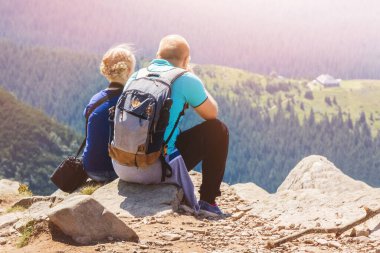Genç adam ve kız, güneşli bir havada dağın tepesinde oturuyor ve doğaya hayran.