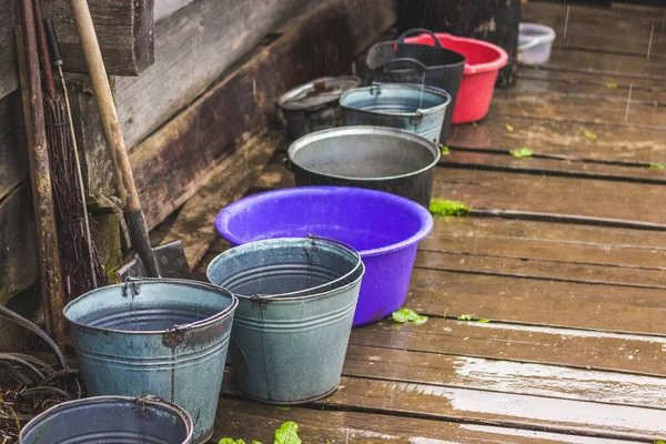 Agricultural equipment under the house in rainy weather. Bucket and bowl on a wood floor