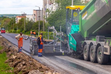 Ukrayna, Khmelnytsky bölgesi, Krasyliv. Mayıs 2021. Asfalt kaldırım taşı asfalt döşeme sırasında yolda ve asfalt kaldırım kovasına asfalt yüklerken araba. Yol tamiri. Yeni bir yol açıyorum