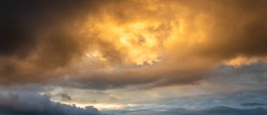 Destansı panoramik manzara, gün batımında ya da gündoğumunda altın yağmur bulutları kara fırtına bulutlarının arasından geçip parlak ışıkla güçlü ilahi bir zemin oluşturur.