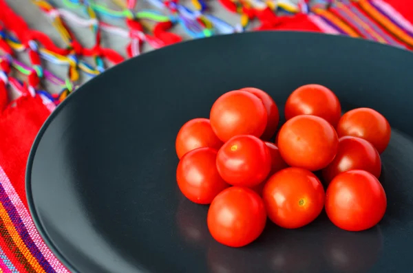 Kirschtomaten auf schwarzem Teller über bunter mexikanischer Tischplatte — Stockfoto