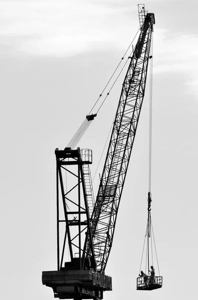 Silhouette of a large tower crane lifting construction workers — Stock Photo, Image