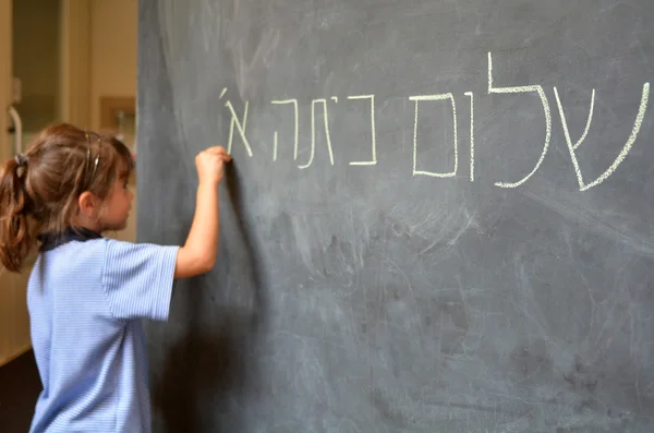 Little girl writes Hello First Grade greetings in Hebrew — Stock Photo, Image