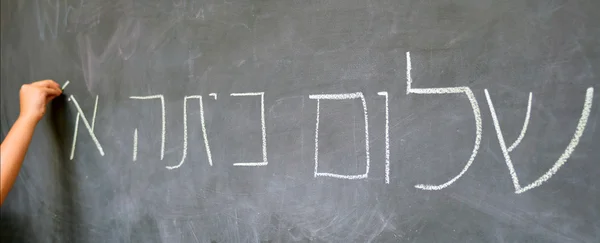 Pequeña mano de niño escribe hola saludos de primer grado en hebreo — Foto de Stock