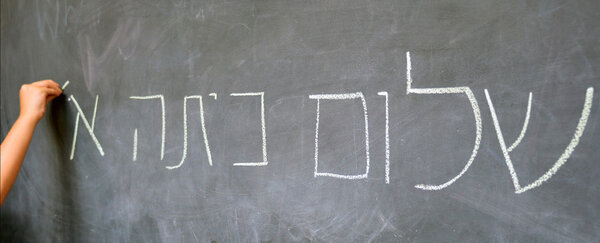 Little child hand writes Hello First Grade greetings in Hebrew 