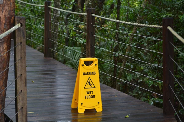 Warning sign for slippery floor on a wooden path of a rain fores