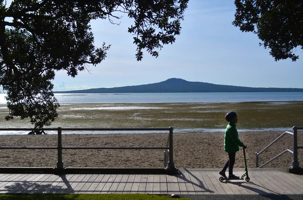 Child ride a scooter against Rangitoto Island — Stock Photo, Image