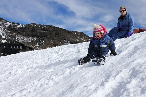 Mutter beobachtet, wie ihr Kleinkind auf Schnee rutscht — Stockfoto