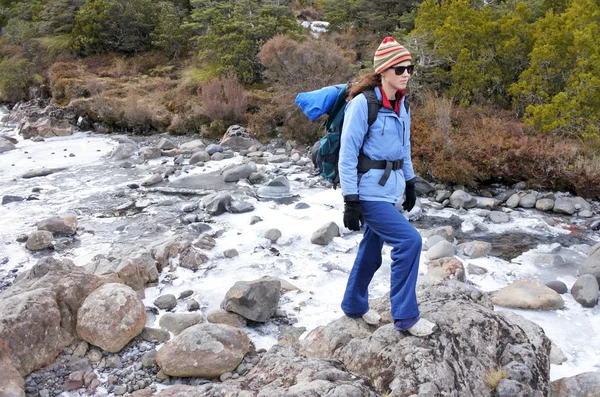 Mujer excursionista cruzando un arroyo congelado — Foto de Stock