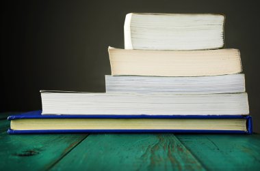 Tahta bir masada yığınla kitap.