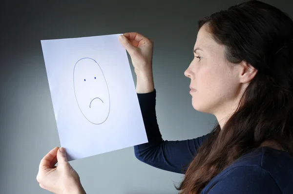 Молодая женщина смотрит на рисунок с грустным лицом — стоковое фото