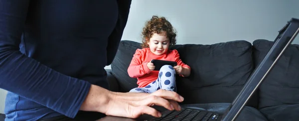 Mère travaille sur un ordinateur portable pendant que son enfant joue sur un smartphone — Photo