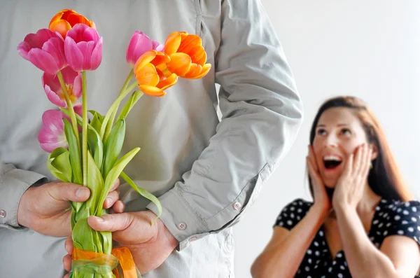 Surprised woman (age 30-35) receive tulip flowers from her lover. Couple relationship concept. copy space