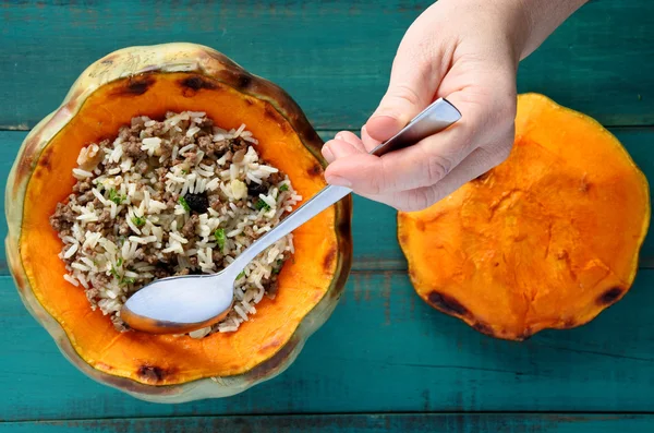 Woman hand with a spoon eat stuffed pumpkin — Stock Photo, Image