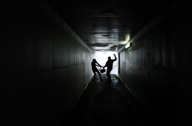 Silhouette of a man thief steals a bag from a woman in a dark tunnel. Violence against women concept. Real people, copy space clipart