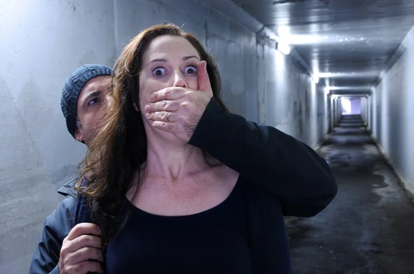 En mann angriper en kvinne bakfra i en mørk tunnel – stockfoto