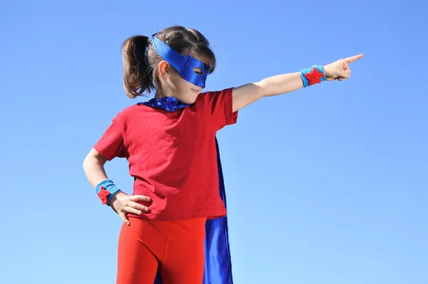 Superhero girl points towards dramatic blue sky — Stock Photo, Image