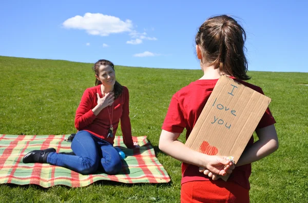 Young girl looks at her mother and  holds behind her back a card — Stock Photo, Image