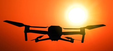 Dramatik günbatımında havada uçan bir dronun silueti. .