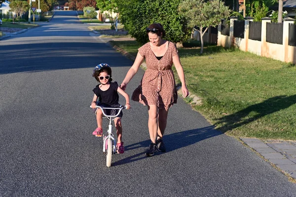 一位年轻母亲教女儿骑自行车在城市街道上的镜头 — 图库照片