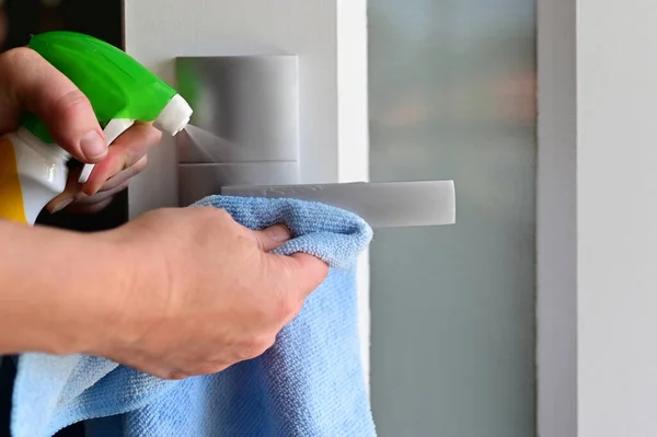 感染拡大を防ぐために自宅のドアハンドル上の洗浄洗剤を噴霧女性の手 — ストック写真