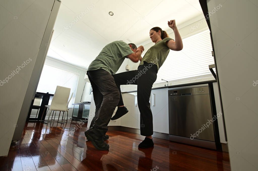 Woman victim using a self defense technique  against a violent man attacker in home kitchen.