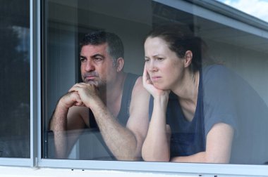 Worried middle aged couple looking through home window. Real people. Copy space clipart