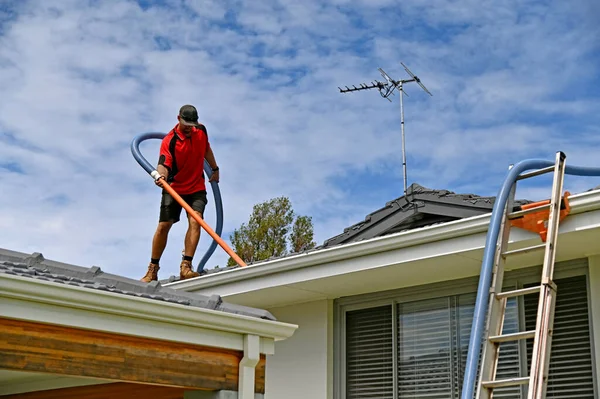 Professional young Gutter cleaner cleaning gutters working on house roof.