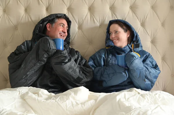 暖かい服を着て毛布で覆われた幸せなカップルは 寒い冬の日に寝室で熱い飲み物を持って お互いを見てダブルベッドに座って — ストック写真