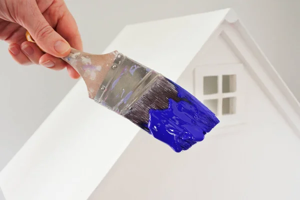 Osoba Trzymająca Pędzel Niebieskim Kolorze Farby Przeciwko Białemu Domowi Remont — Zdjęcie stockowe