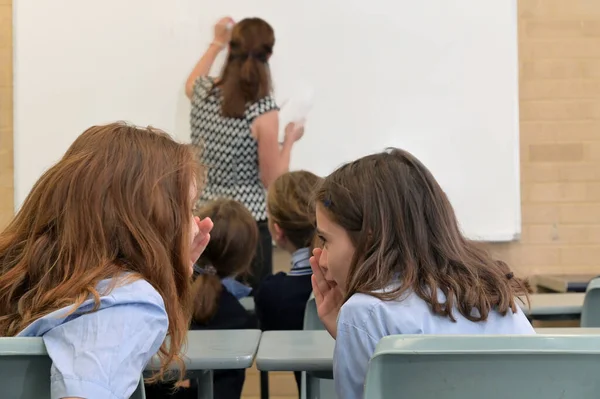 Two School Girls Whispering Secrets Classroom Teachers Back — Stock Photo, Image