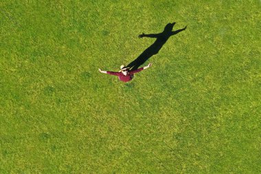 Yeşil çimlerin üzerinde kollarını açmış gökyüzüne bakan mutlu, aktif bir kadının havadan görüntüsü..