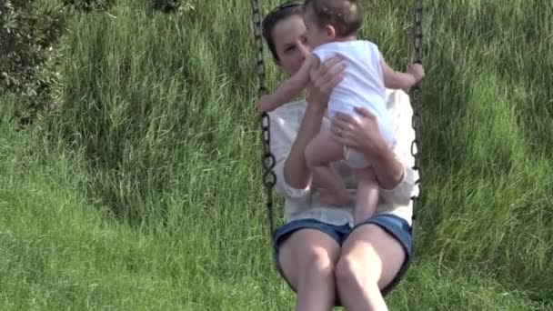 Ung mamma och hennes barn gunga tillsammans i lekparken — Stockvideo