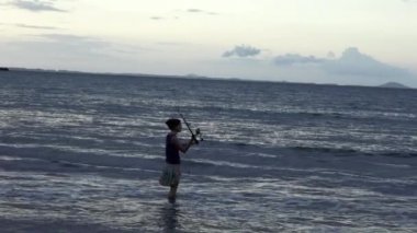 Young woman casting rod fishing from the beach at sunset