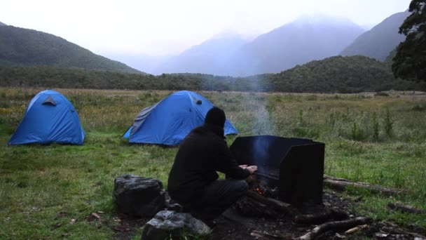 Hiker warms up over an outdoor campfire — Stock Video
