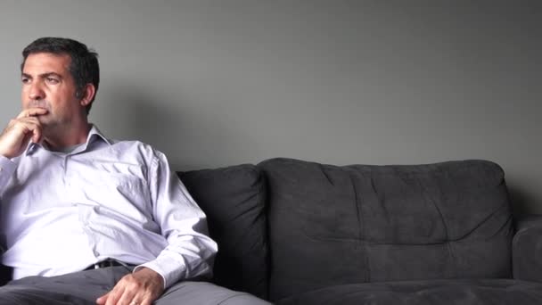 Man i fyrtioårsåldern sitter på en soffa upprörd — Stockvideo