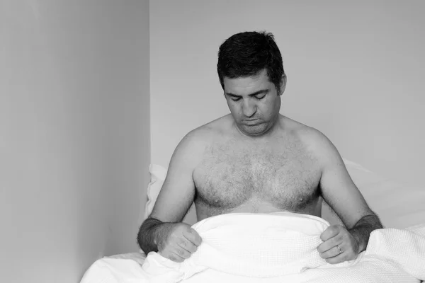 Upset man in his forties (40s) in bed looking down at his penis — Stockfoto