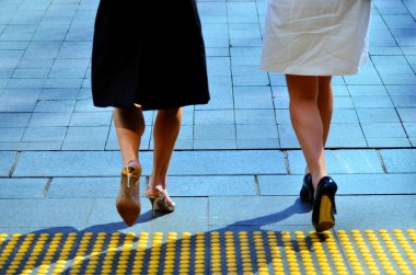 Young business women legs walking on city street together.