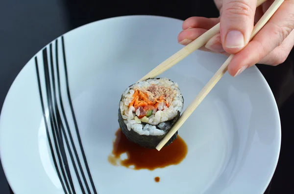 Mulher mão segura um Makizushi sushi fresco maki rolo com chopst — Fotografia de Stock