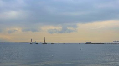 Deniz fenerinin yanında, bulutlu bir gökyüzünün altında sakin bir denizin üzerinde uçan bir martı..