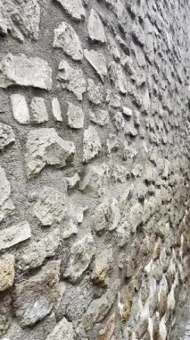 Eski taş duvar dokusuna dikey olarak yakın çekim, pürüzlü duvarcılık detaylarıyla. Dikey kompozisyonda doğal mimari arkaplan tasarım, inşaat ve miras temaları için idealdir.