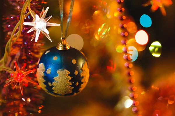 Niebieski cacko w Boże Narodzenie drzewo otoczone kolorowymi światłami — Zdjęcie stockowe