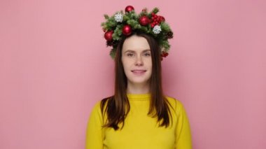 Beni geri ara. Noel çelenginde gülümseyen çekici genç bir kadın bana geri dönüş işareti yapıyor, rahat sarı bir kazak giyiyor, pembe stüdyo arka planının üzerinde duruyor. Mutlu yıllar konsepti