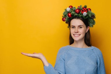 Çekici gülüşü olan neşeli kadın avuç içlerini sarı fotokopi odasına kaldırıyor, yana bakıyor, Noel çelengi giyiyor ve rahat bir süveter giyiyor, bir şeyler gösteriyor. Mutlu yıllar, mutlu yıllar.
