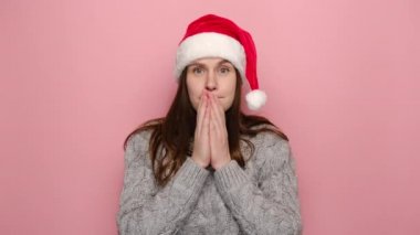 Noel Baba şapkası takmış neşeli genç bir kadın bana kim olduğumu sorar. Evet, kışlık gri süveter giymiş, pembe stüdyo geçmişinde izole edilmiş. Mutlu yıllar ve Xmas konsepti