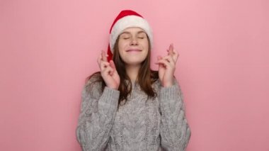 Güzel genç kadın elleri dua ederken kıvrılmış parmaklarını çapraz tut dilek tut, kışlık süveter ve Noel Baba şapkası giy, pembe stüdyo arka planında izole edilmiş. Xmas geliyor.